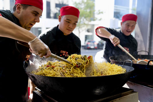 Three people cooking over large woks