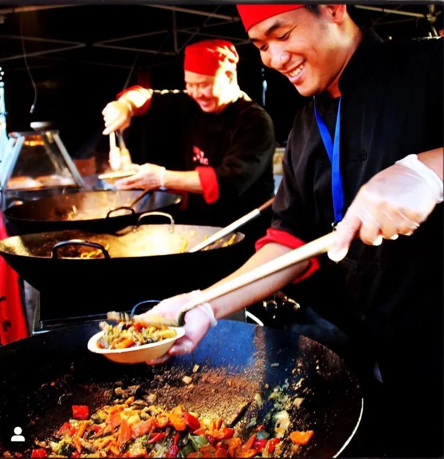 Flying Woks chef serving stir fry from giant wok at a night event